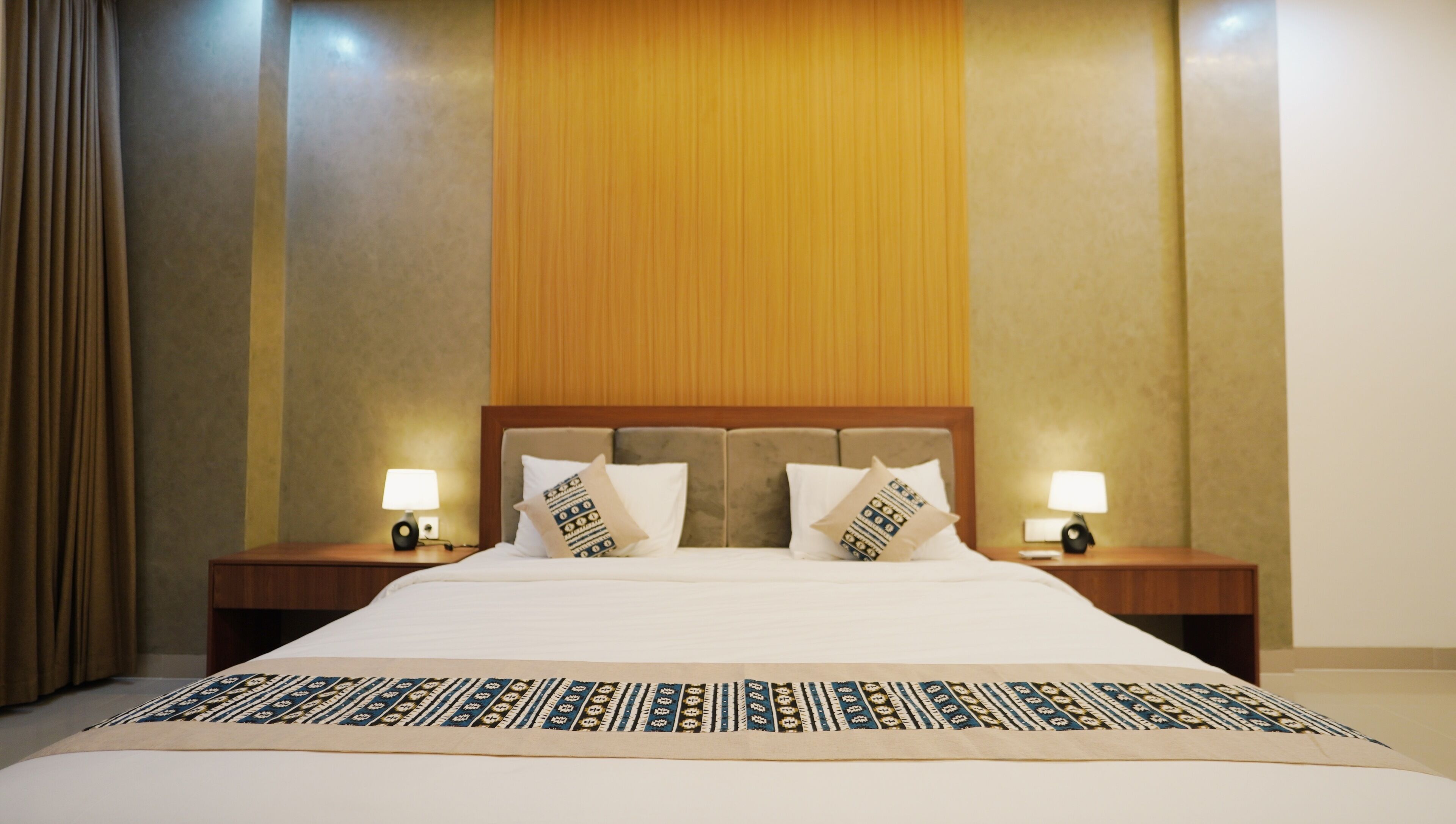 A hotel room with a large bed, two bedside tables with lamps, and a patterned bedspread.