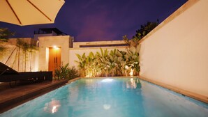 A swimming pool with a wooden deck and a bench, surrounded by plants and a white wall. - SLOKAYANA VILLAS (Pecatu)