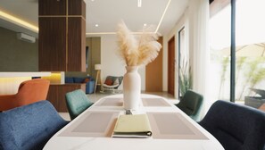 A modern hotel room with a dining table, chairs, a vase with feathers, and a view of the outdoors. - SLOKAYANA VILLAS (Pecatu)