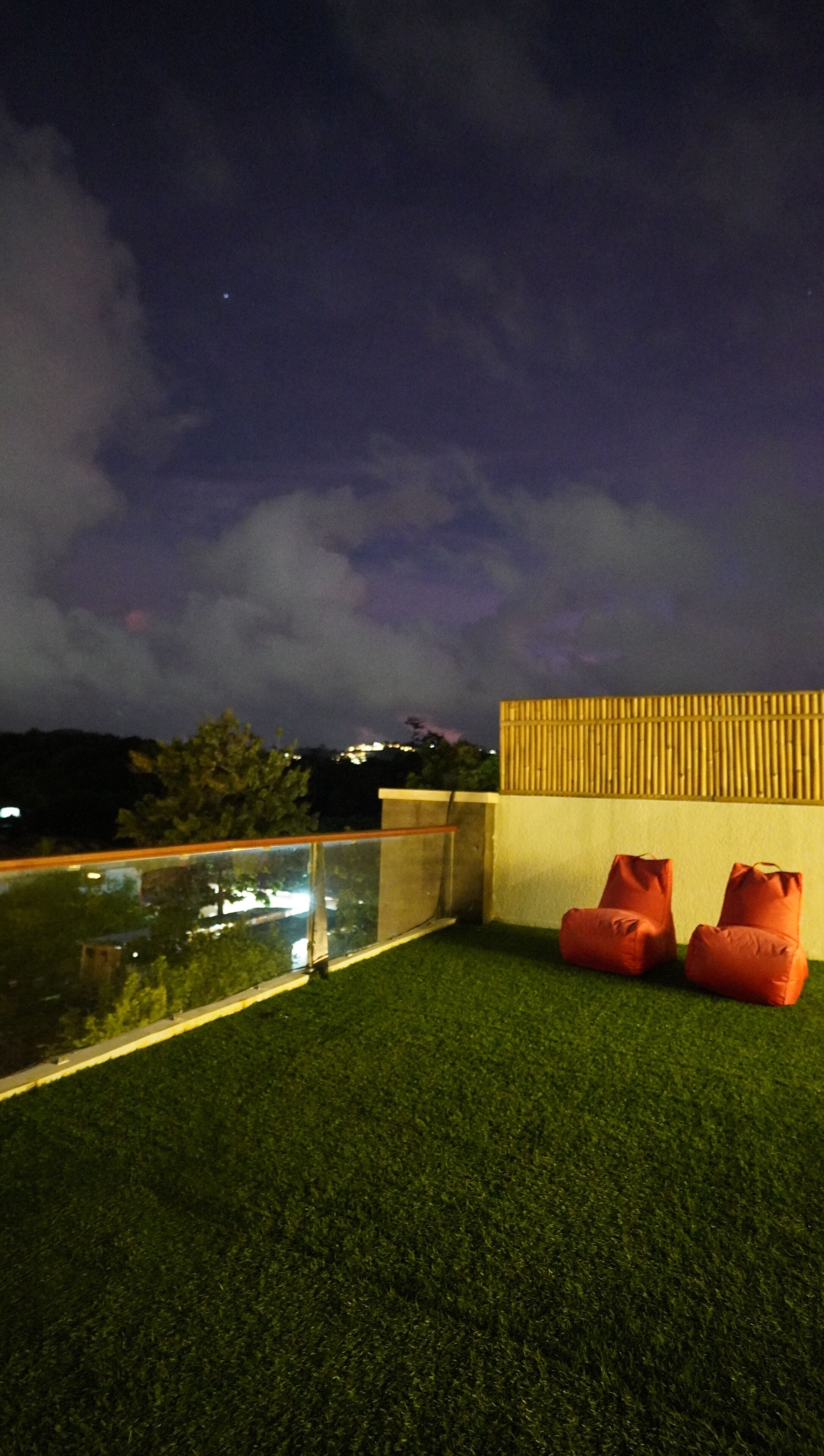 A rooftop terrace with artificial grass, a railing, and two orange poufs.