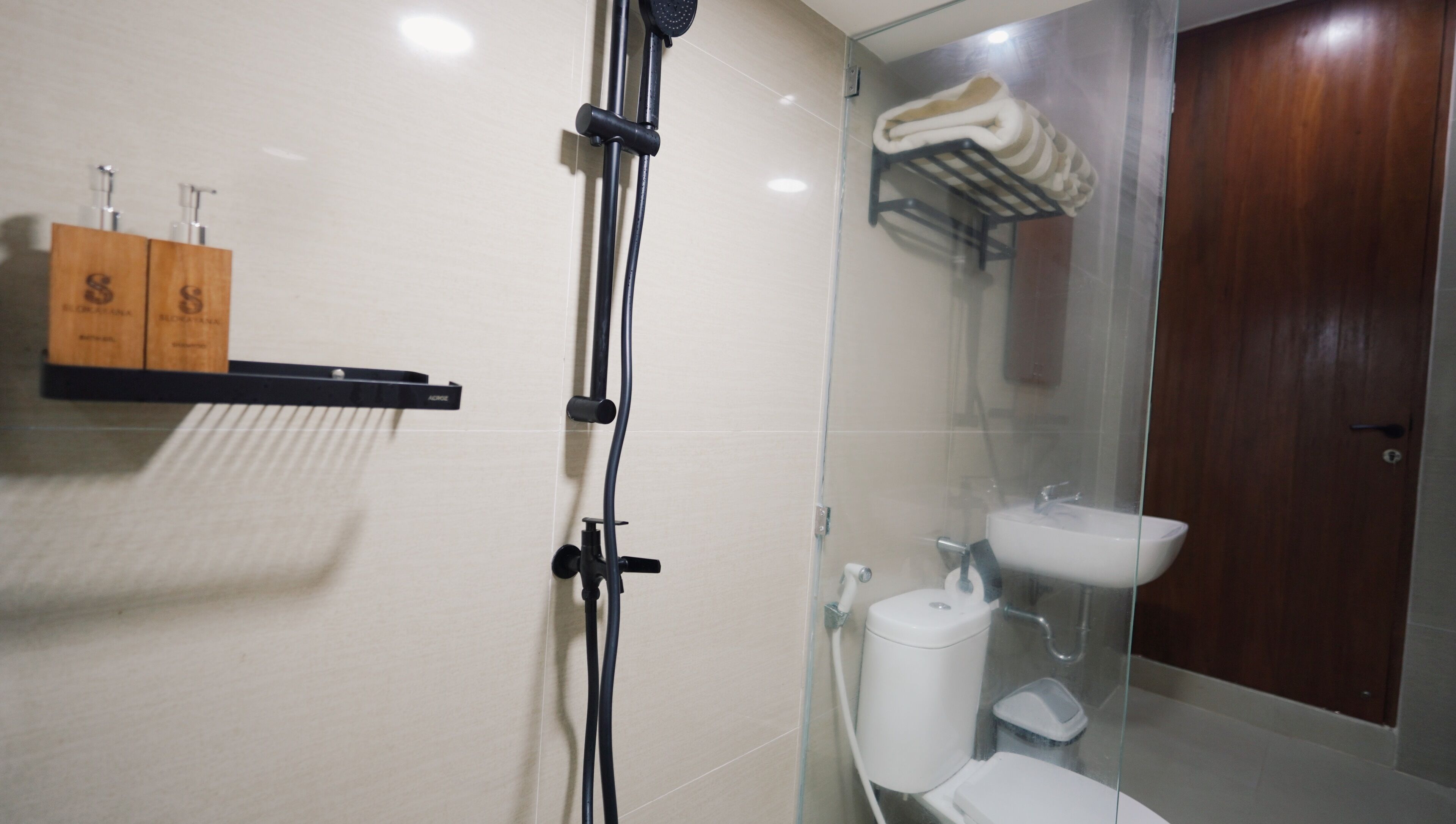 Un bagno moderno con box doccia in vetro, vaso sanitario bianco, lavabo in vetro e ripiano in legno con articoli da toilette.