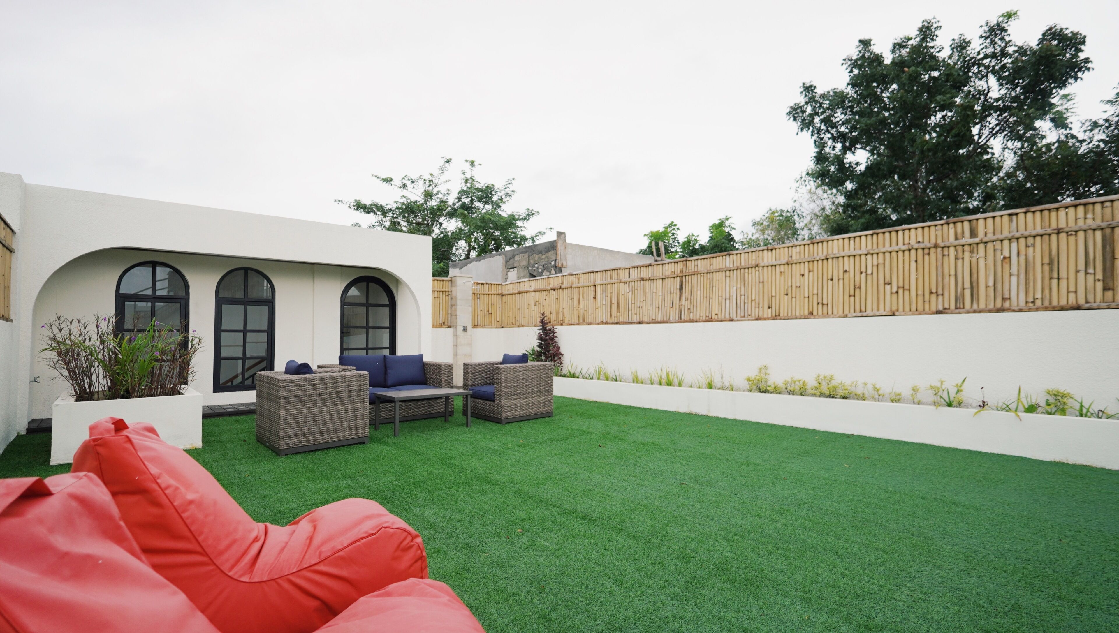 A modern outdoor patio with artificial grass, wicker furniture, and a red bean bag.