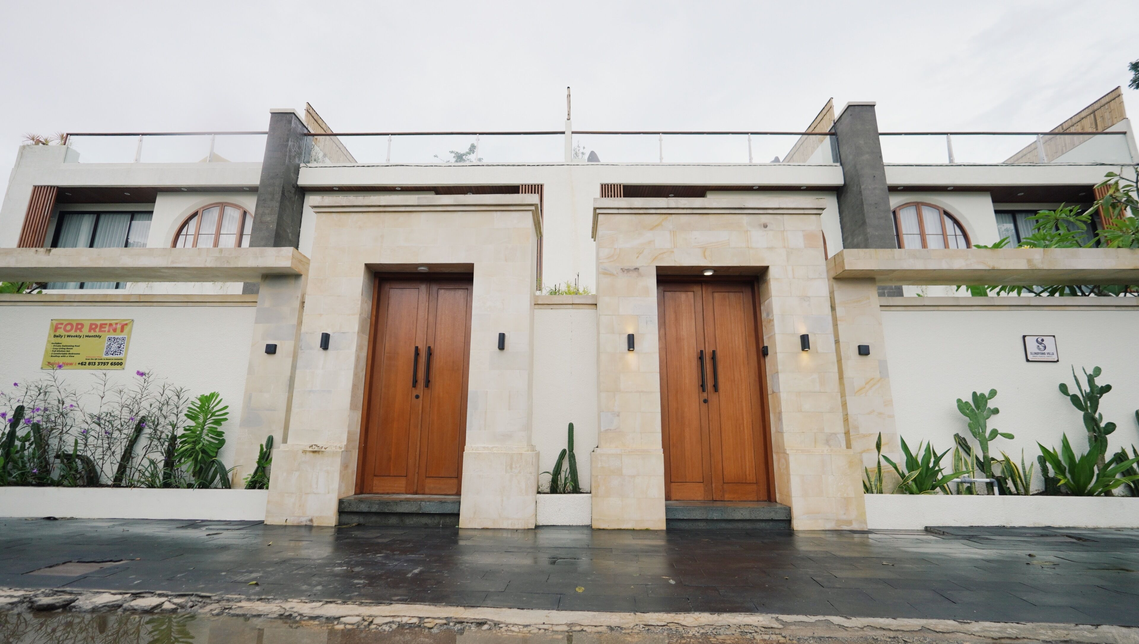 A modern building with two symmetrical wooden doors, a balcony, and a sign indicating availability for rent.