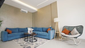 A modern living room with a blue sofa, a small round coffee table, a floor lamp, and a rocking chair. - SLOKAYANA VILLAS (Pecatu)