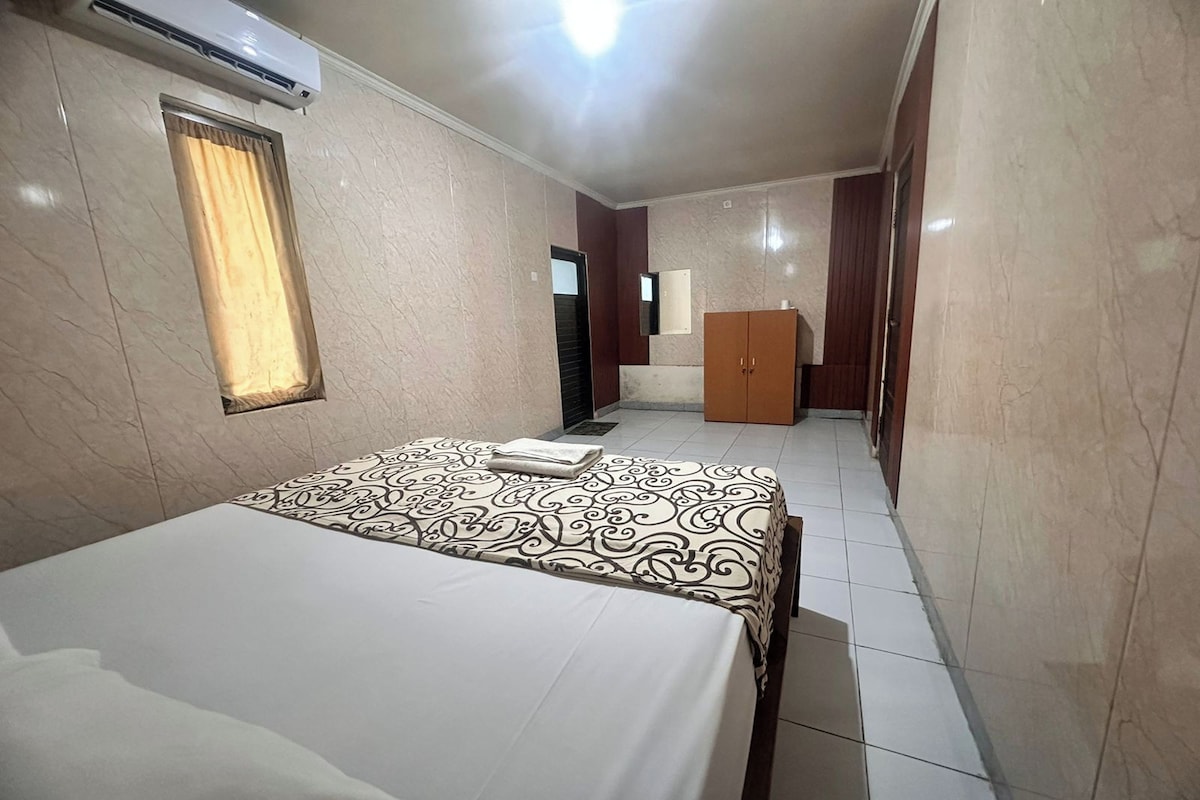 A hotel room with a bed, a wardrobe, an air conditioning unit, and a mirror.