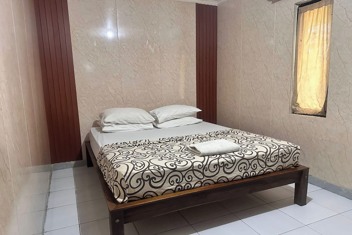 A neatly made bed with a patterned bedspread, a wooden headboard, and a window with a curtain.