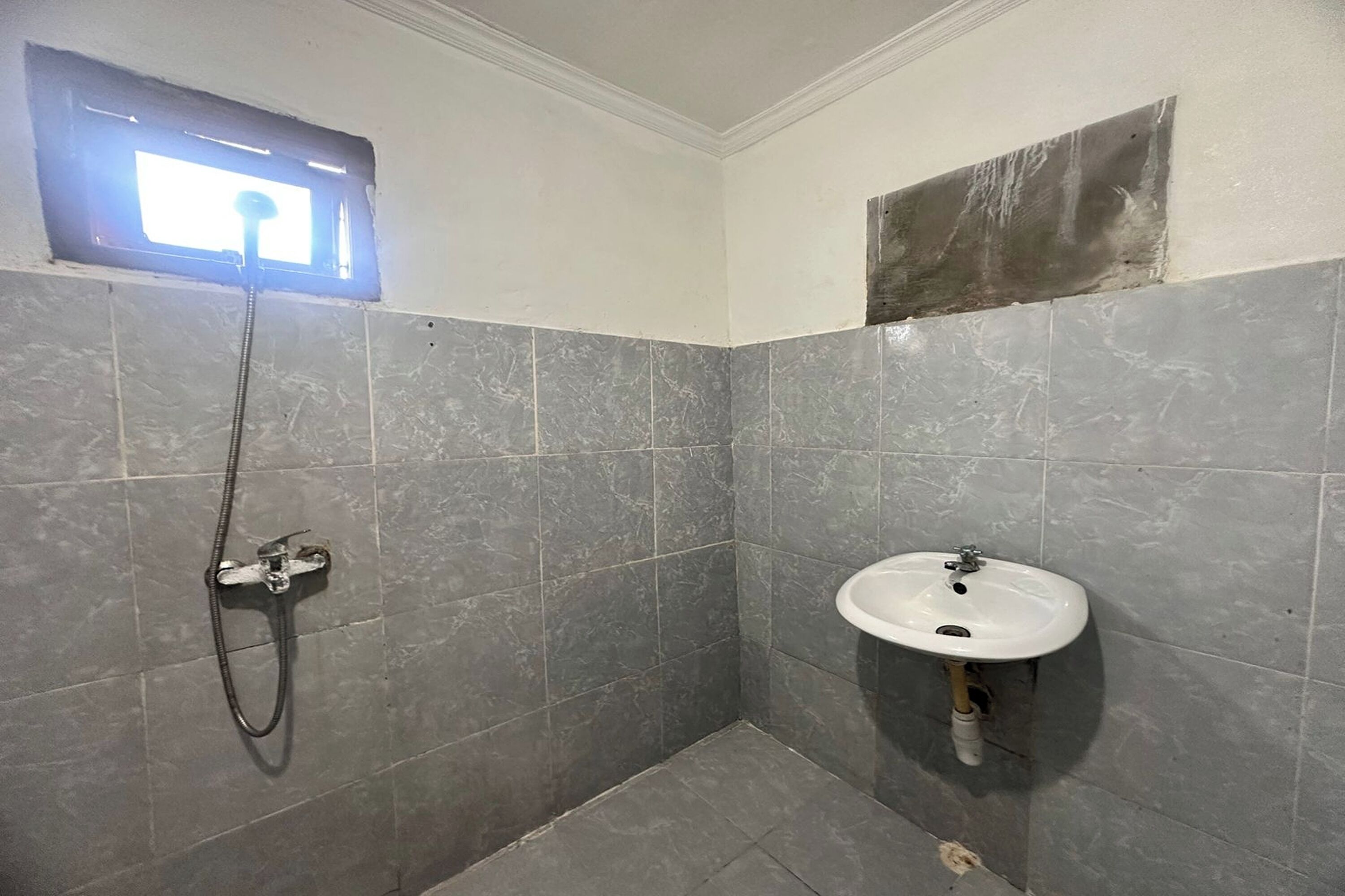 A bathroom with grey tiles, a shower, and a sink.