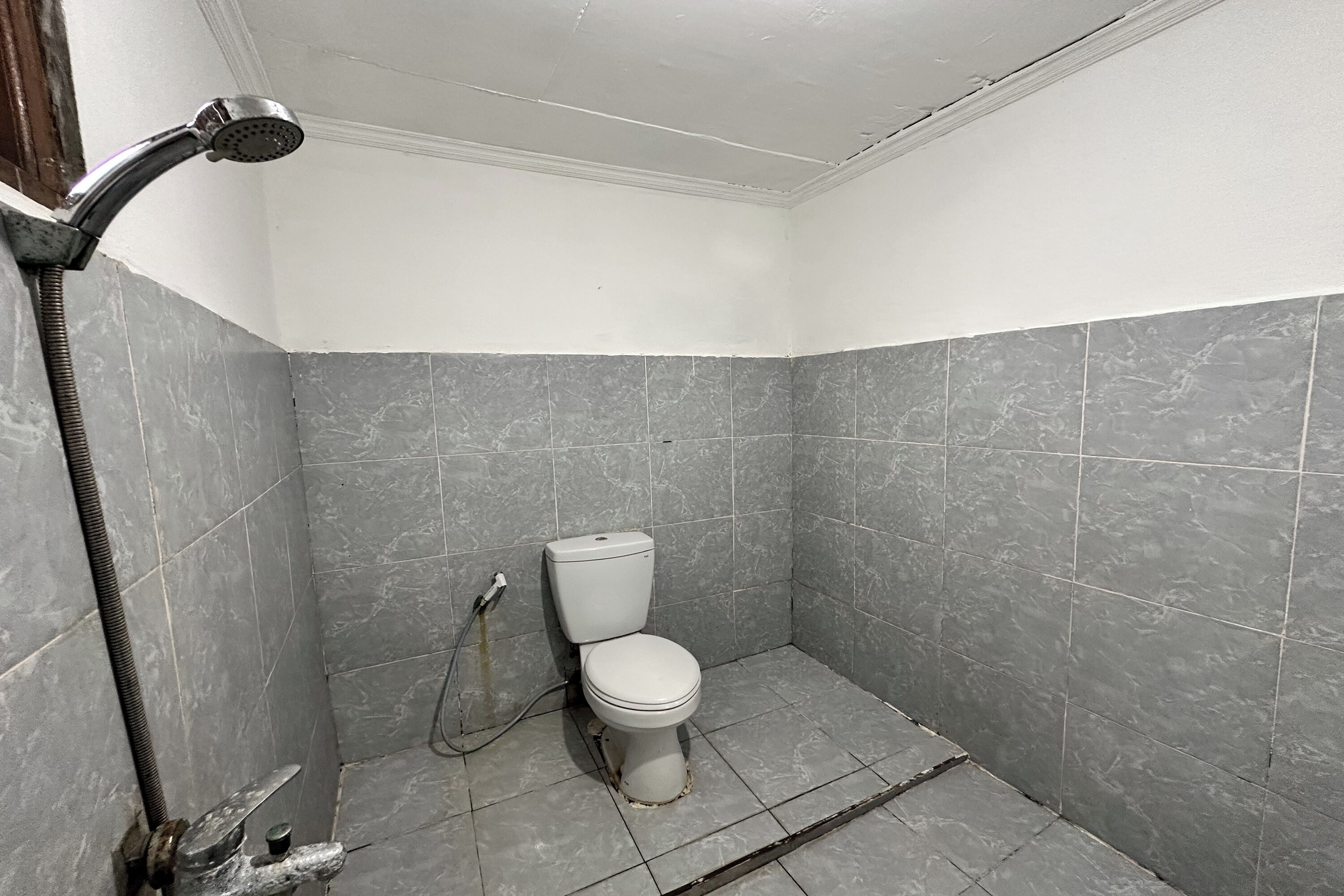 A small, tiled bathroom with a shower, toilet, and a visible pipe.