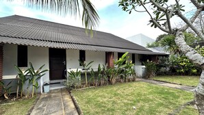 A single-story house with a corrugated metal roof, a front porch, and a well-maintained lawn. - BB Homestay Two (Pecatu)
