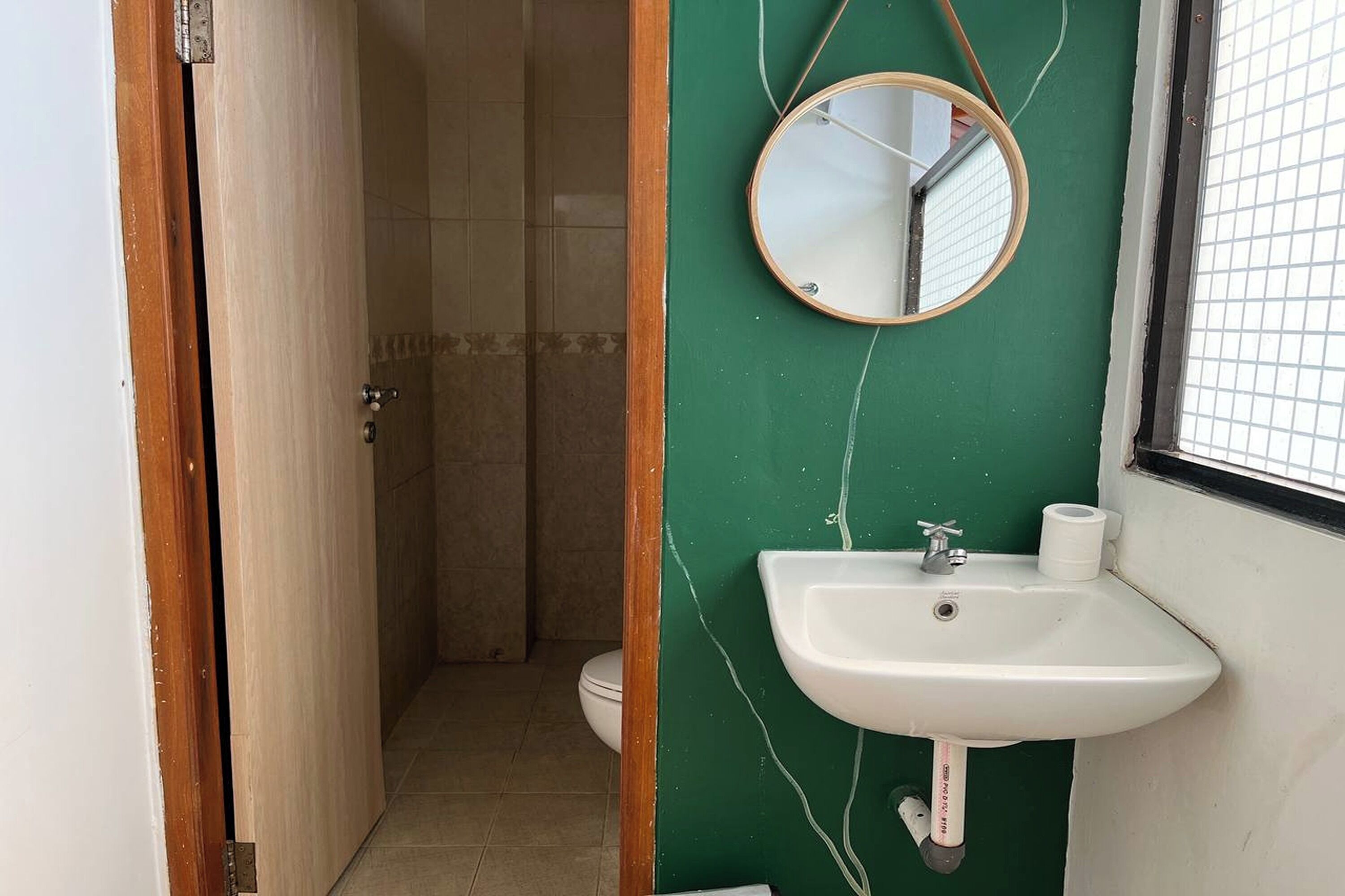 A bathroom with a green wall, a white sink, a mirror, and a toilet.