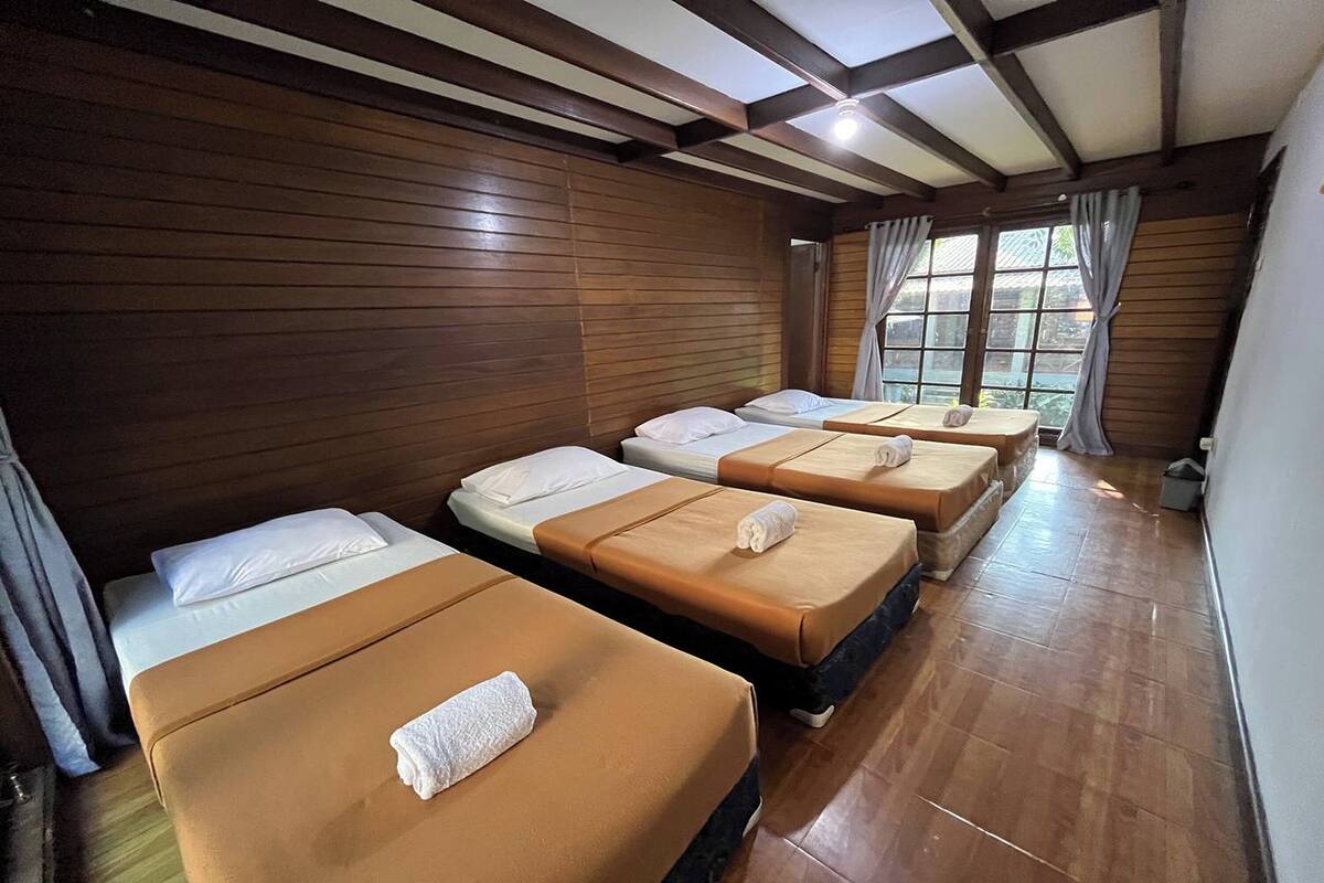 Una habitación con cuatro camas alineadas, paredes de madera y un ventanal con cortinas.