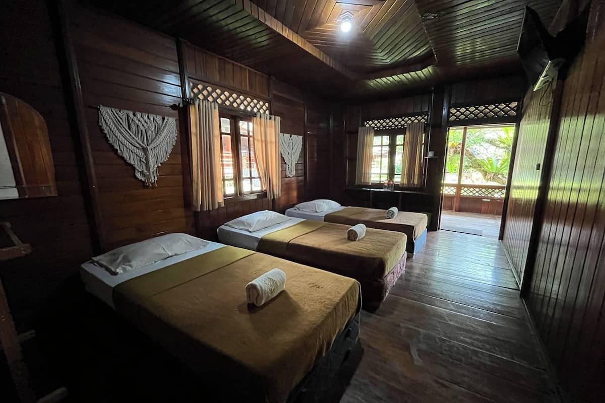Habitación con paredes y suelos de madera, con tres camas con sábanas blancas y cabeceros marrones.