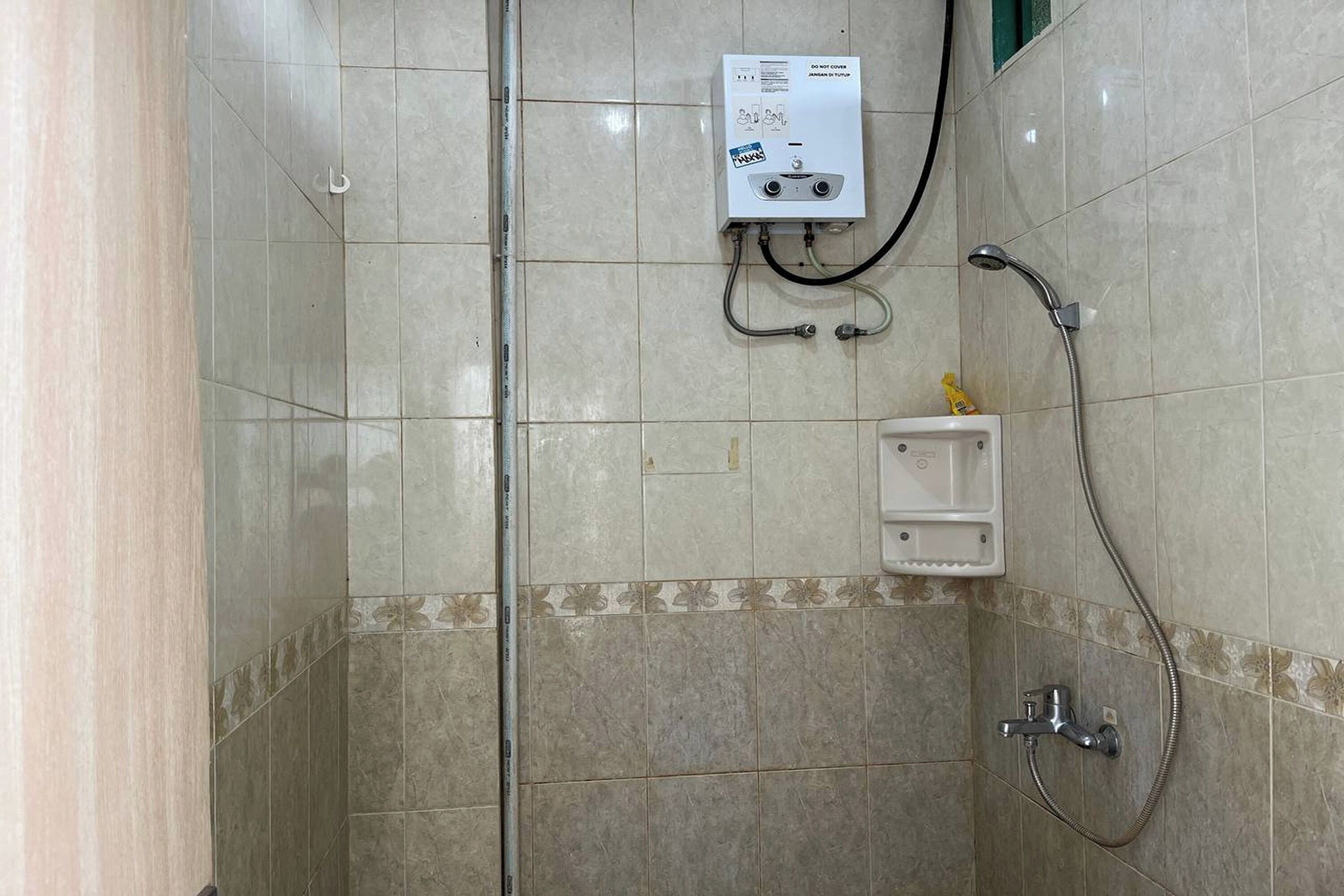 A shower area with a wall-mounted heater, a handheld showerhead, and a small shelf with toiletries.