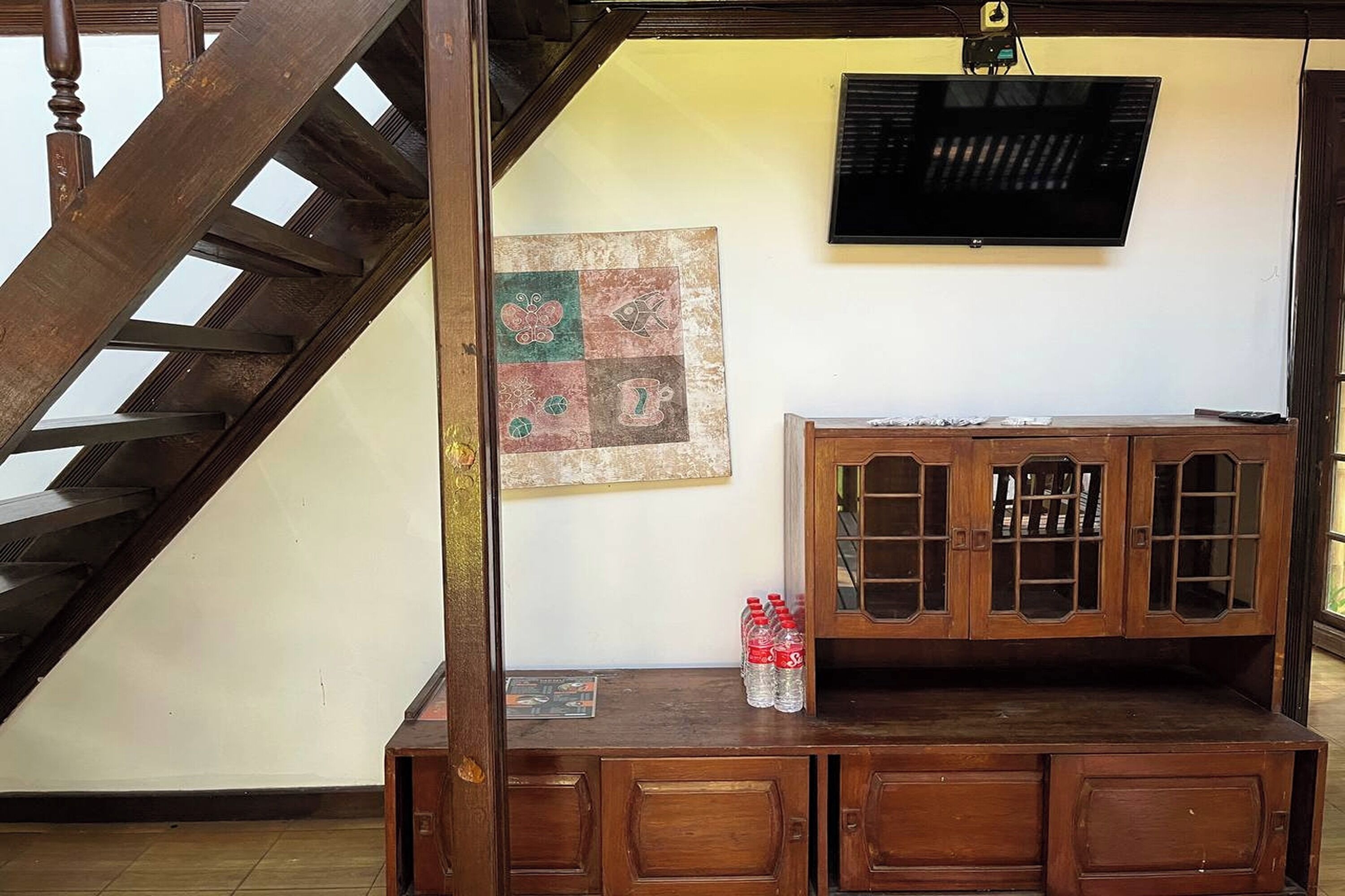 A wooden staircase leading to a landing with a cabinet and a television mounted on the wall.