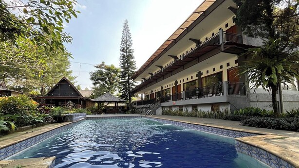 A swimming pool with a tiled edge, surrounded by a building with balconies and a covered area. - Santa Monica Resort (Caringin)