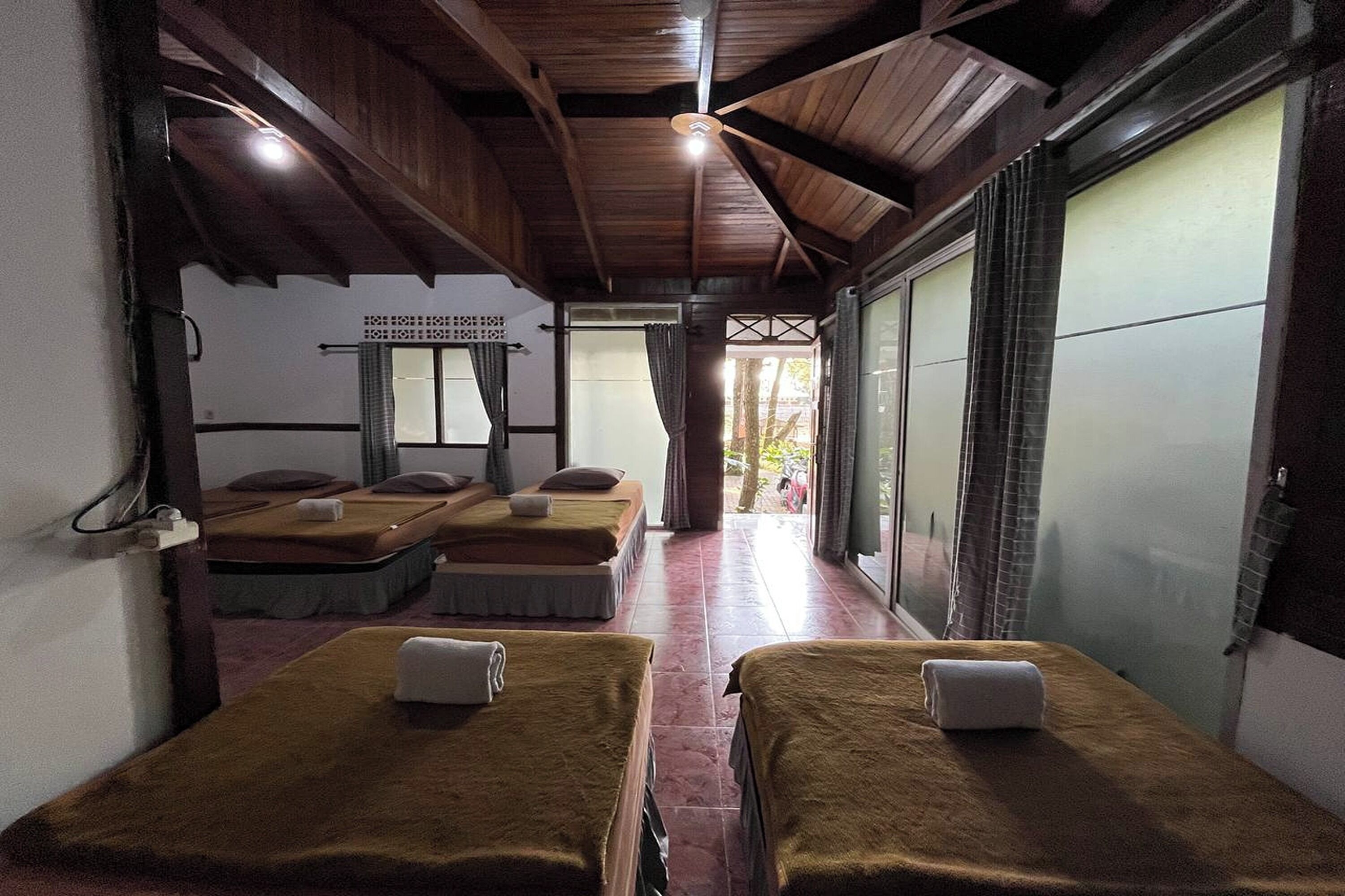 A room with two beds, a wooden ceiling, and a view through a large window.