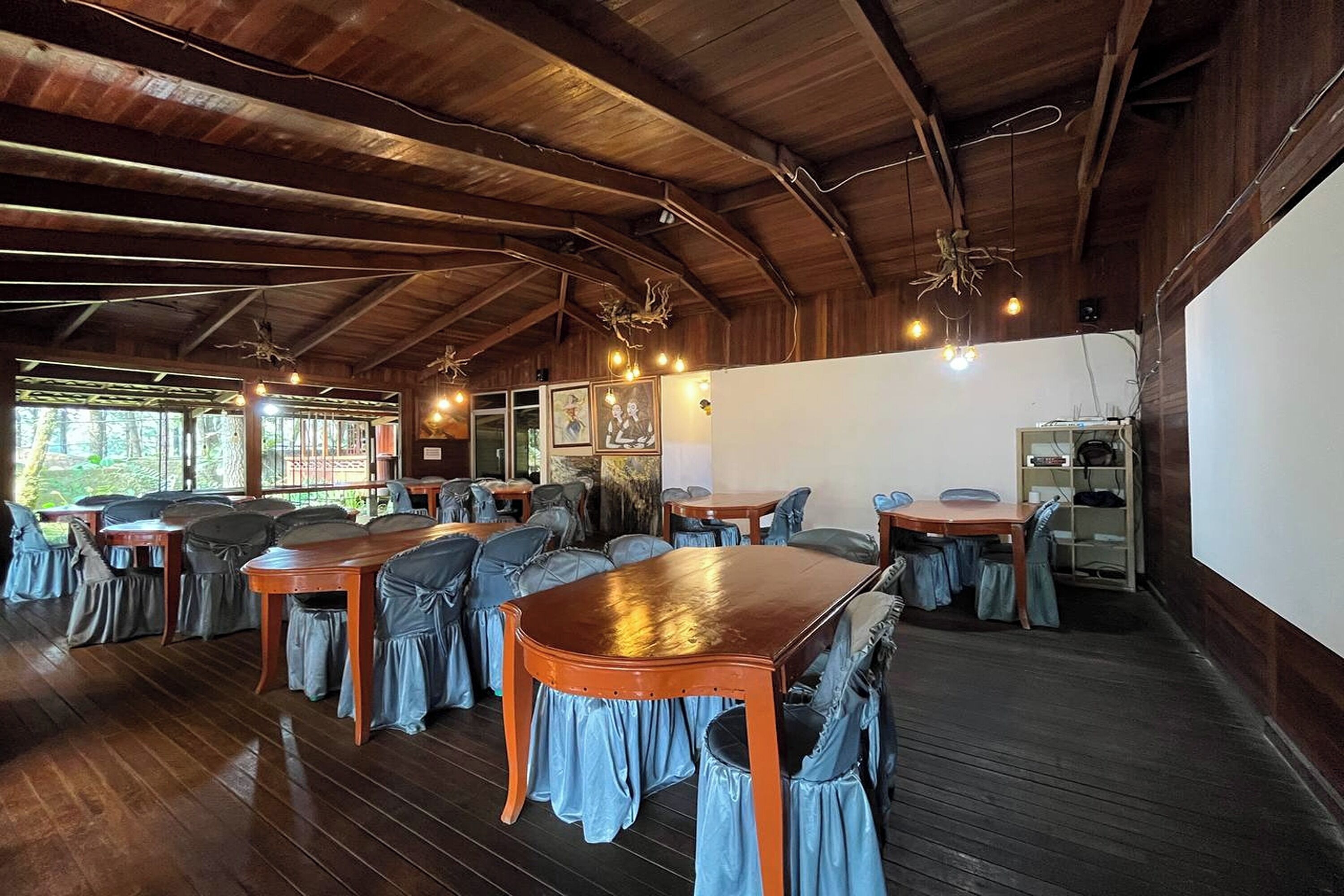 Un comedor amplio con mesas y sillas de madera, ventanas grandes y un techo alto con vigas a la vista.