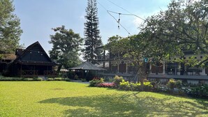 A traditional wooden building with a sloped roof, surrounded by a well-maintained lawn and various trees. - Santa Monica Resort (Caringin)