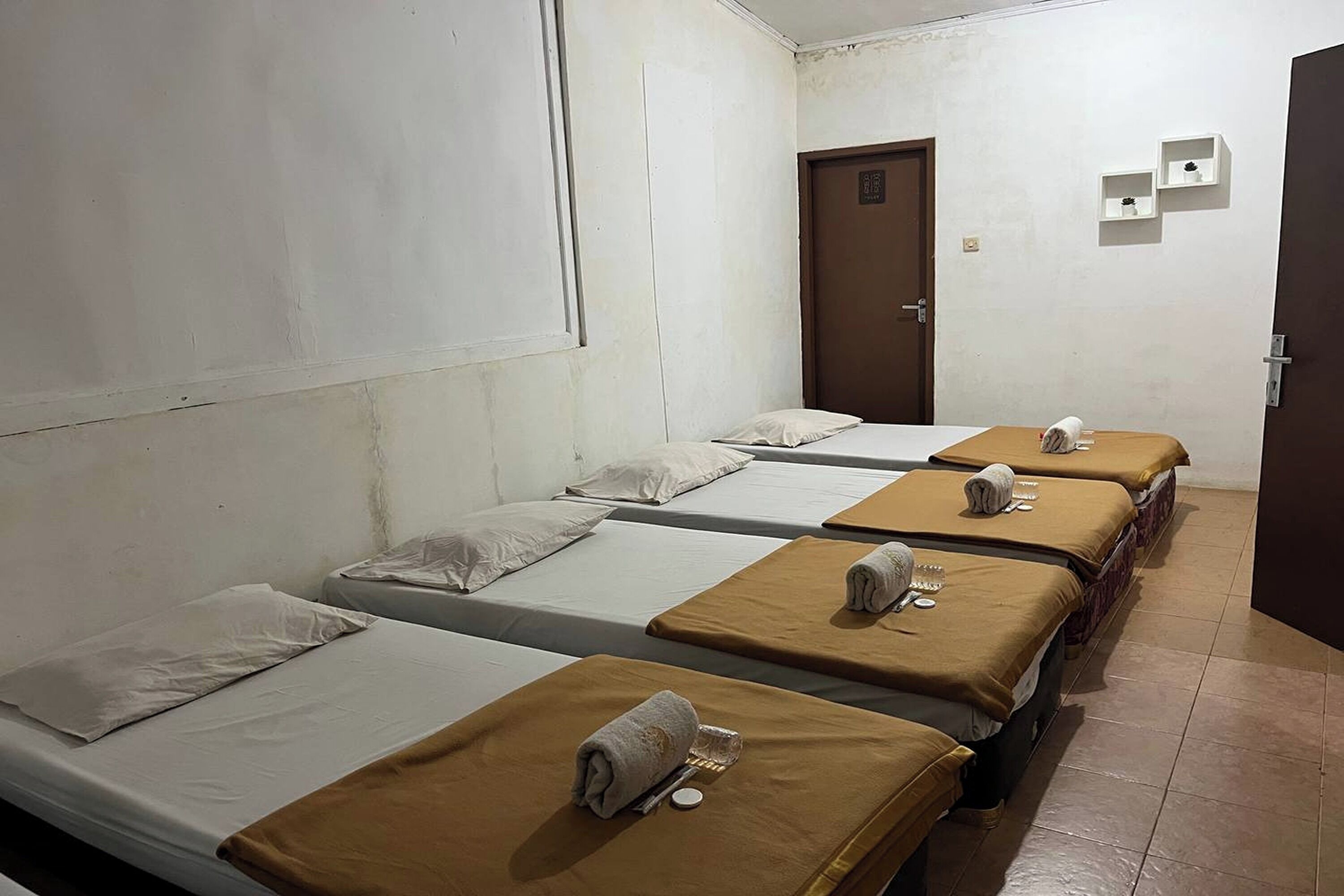 A dormitory room with four single beds, each with a brown blanket and a rolled towel.