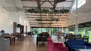 Un amplio espacio interior con varias mesas y sillas, una recepción y plantas colgantes.