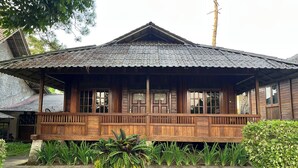 Una casa de madera tradicional con techo de tejas, un porche con barandillas de madera y una planta en maceta al frente.