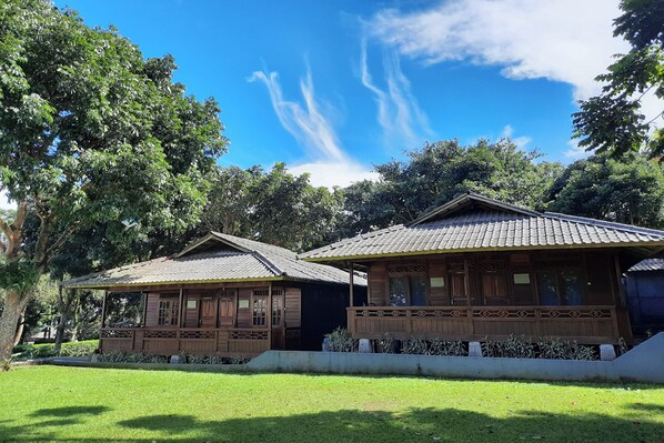 Two wooden buildings with tiled roofs, surrounded by lush greenery and a clear blue sky. - Tjapoeng Resort Pancawati (Caringin)