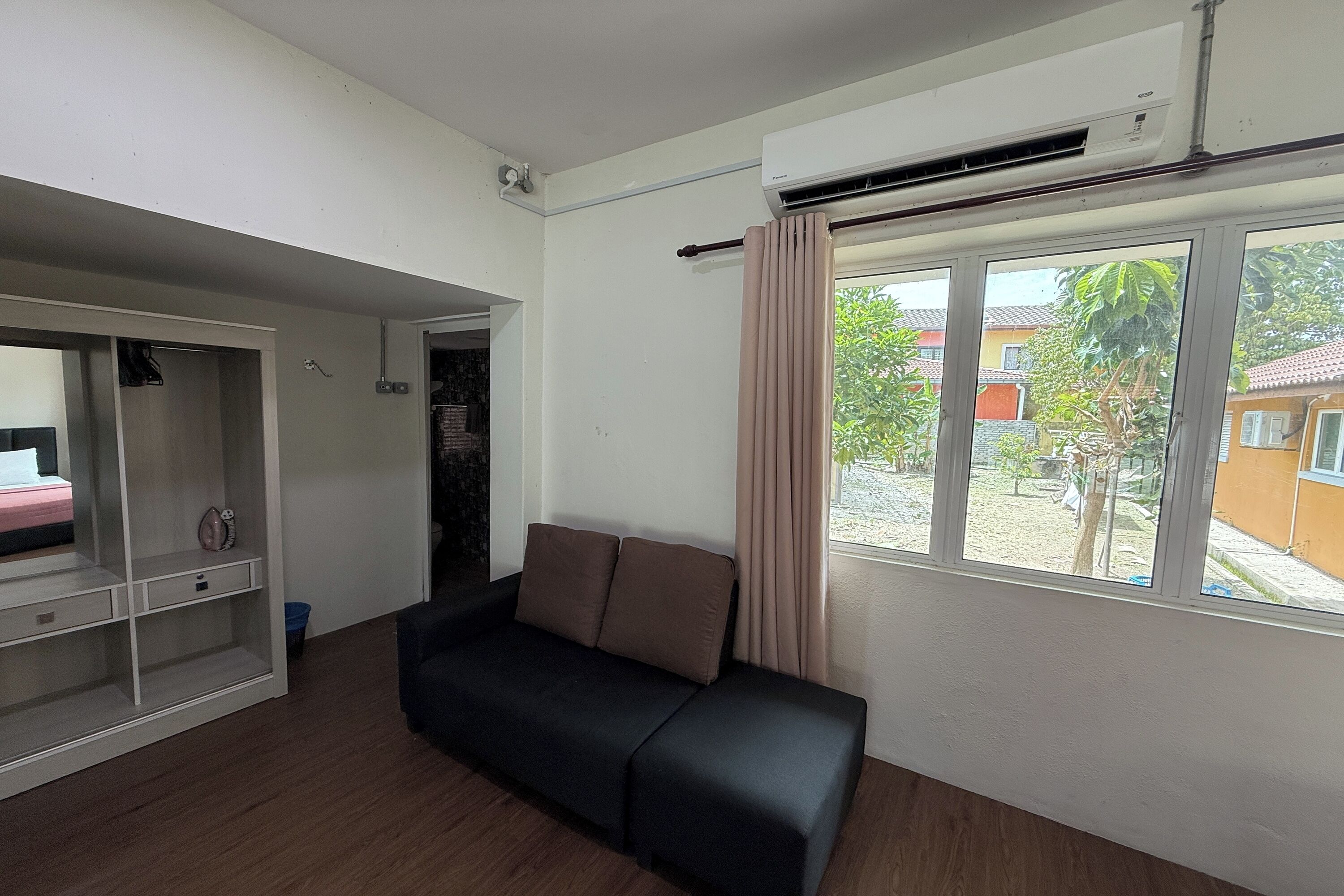 A modern living room with a black sofa, a white entertainment unit, and a large window with a view of the outside.