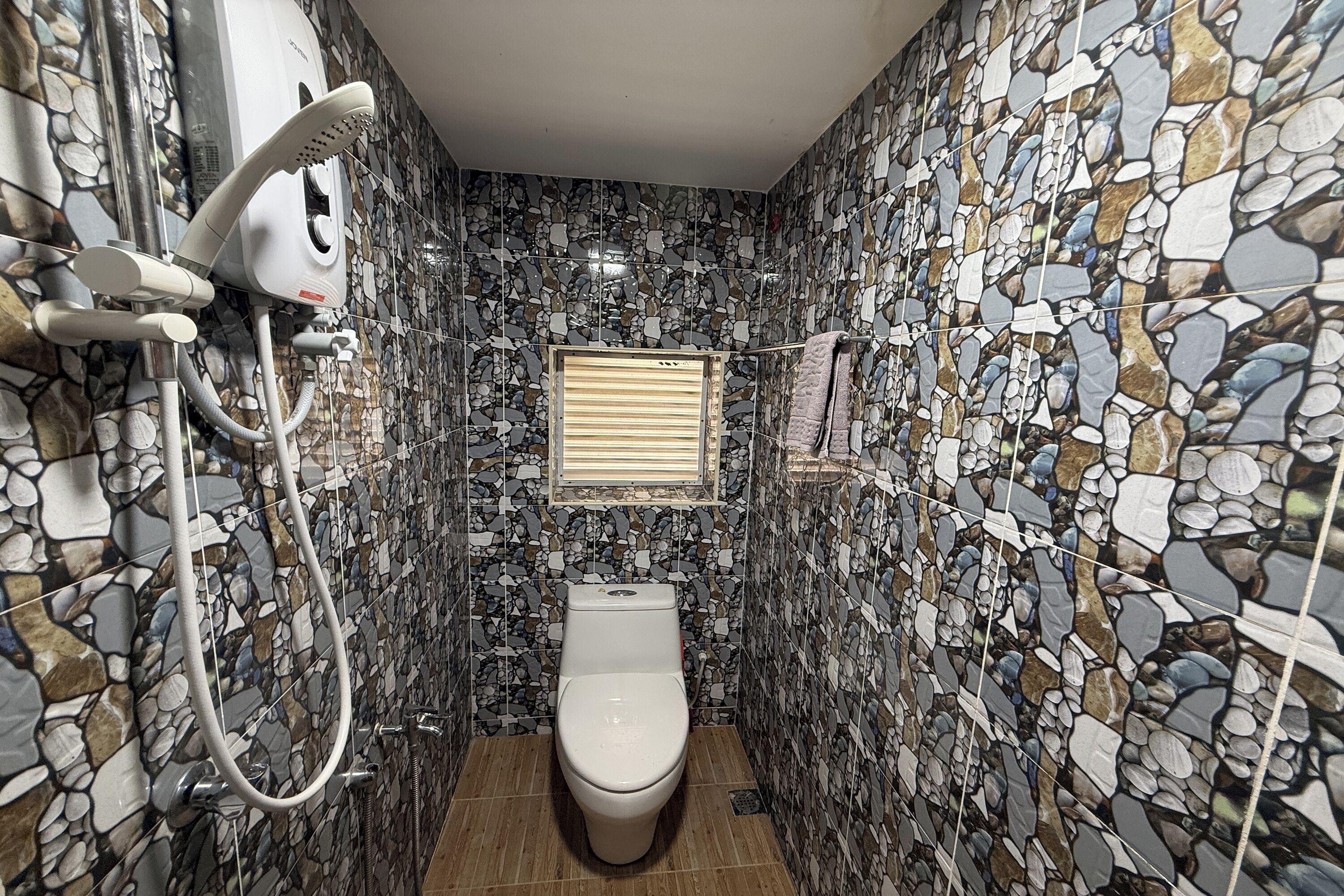 Un baño con pared de mosaicos, inodoro, ducha de mano y barra para toallas.
