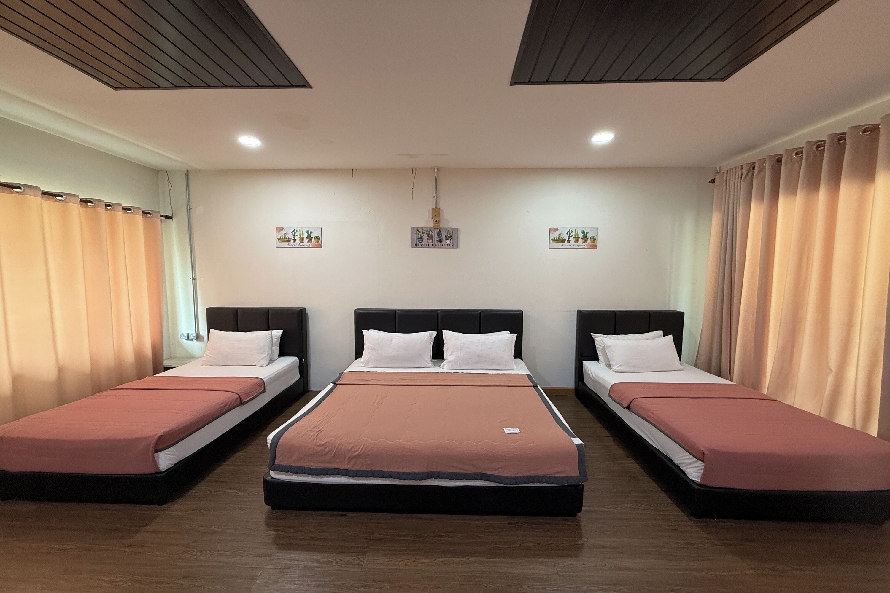Een hotelkamer met drie eenpersoonsbedden, een groot bed, houten vloeren en een plafond met inbouwverlichting.