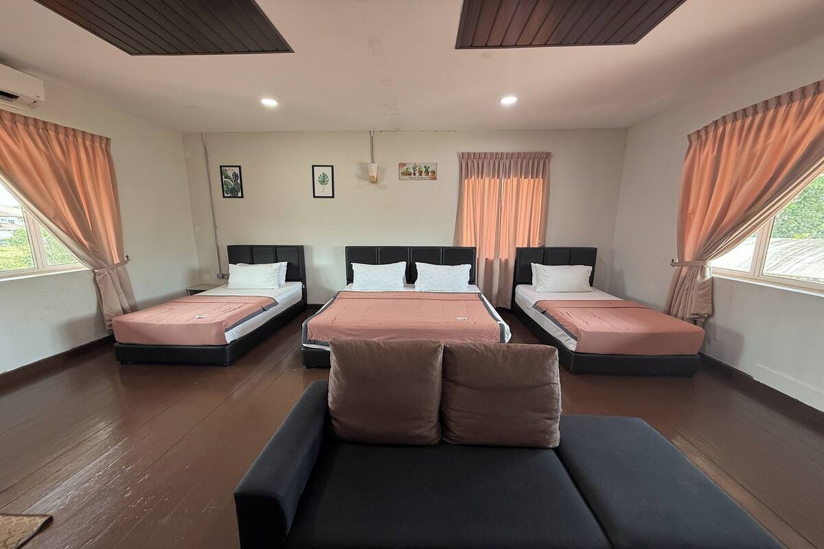 A hotel room with three single beds, a sofa, and a large window with curtains.