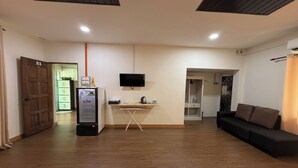 A room with a wooden floor, a black sofa, a small table with a kettle, a TV mounted on the wall, and a door labeled B1. - Inapan Taman Herba (Kepala Batas)