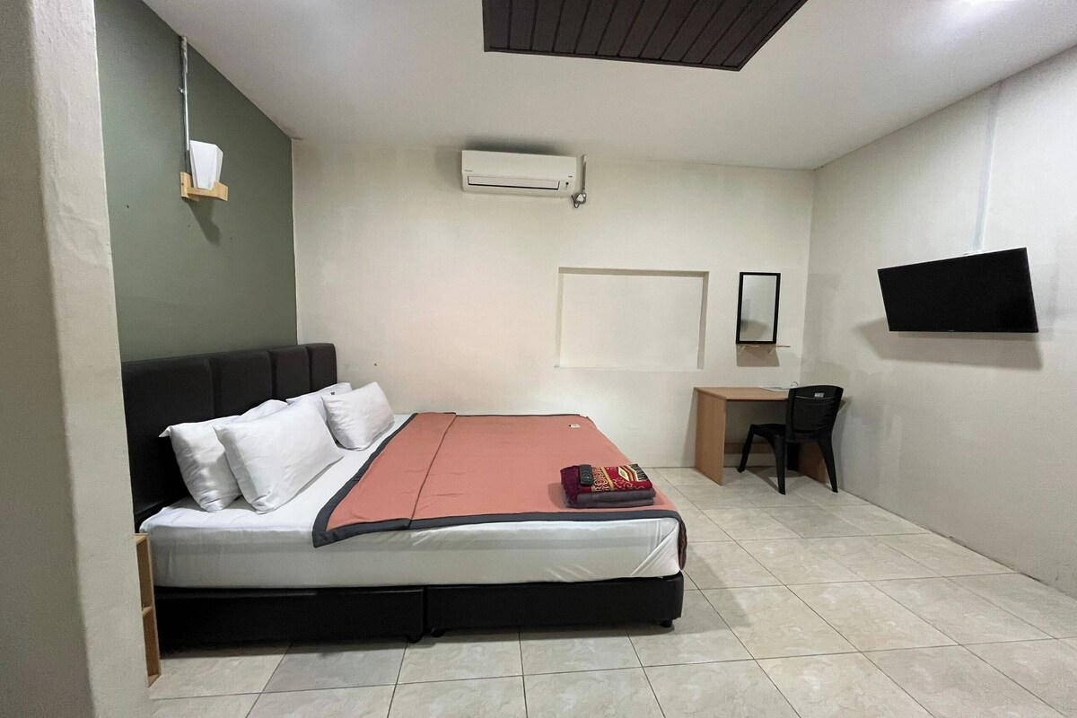 A bedroom with a bed, a desk, a chair, a TV, and an air conditioning unit.