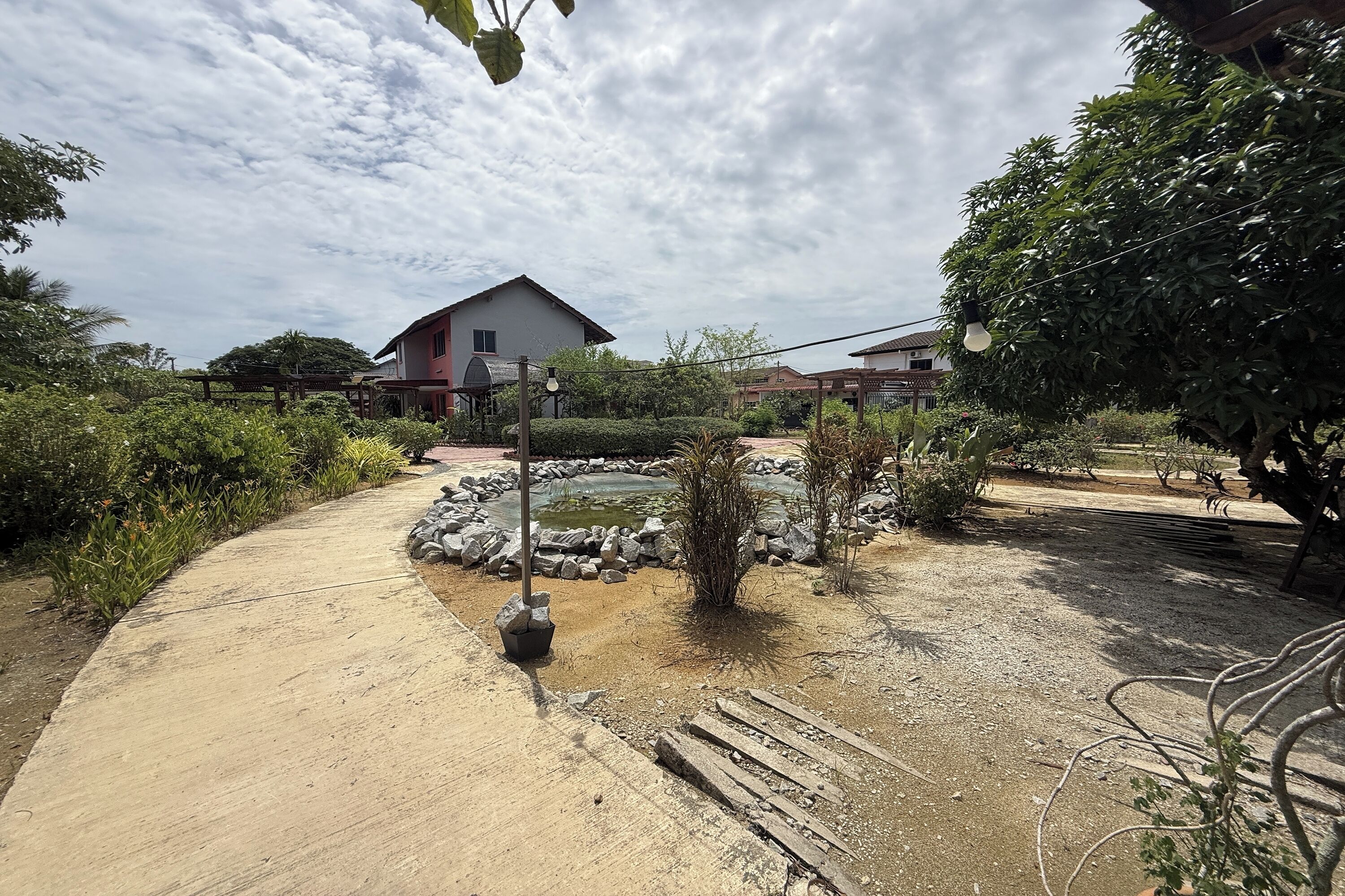 Caminho de jardim que leva a um lago, com uma casa ao fundo.
