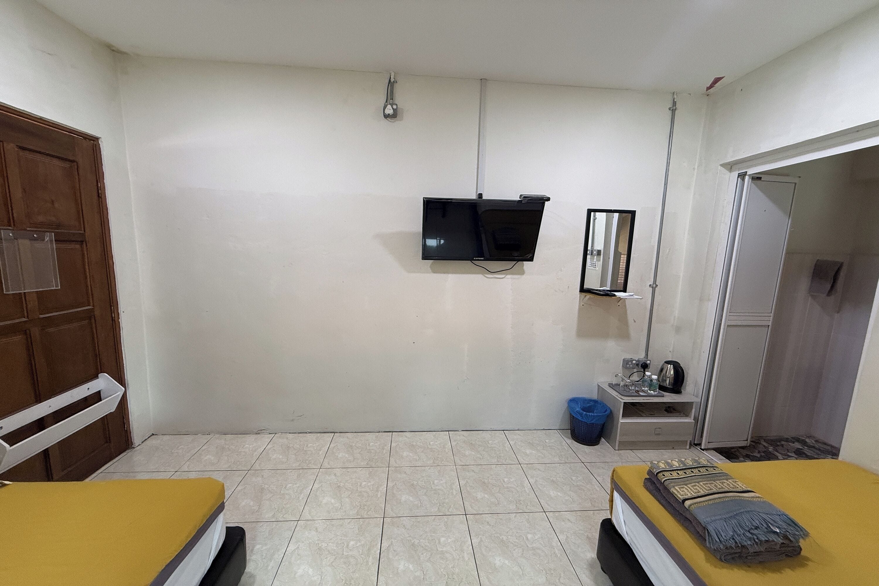 A small, clean room with two beds, a TV, a mirror, a wardrobe, and a small table with a kettle.