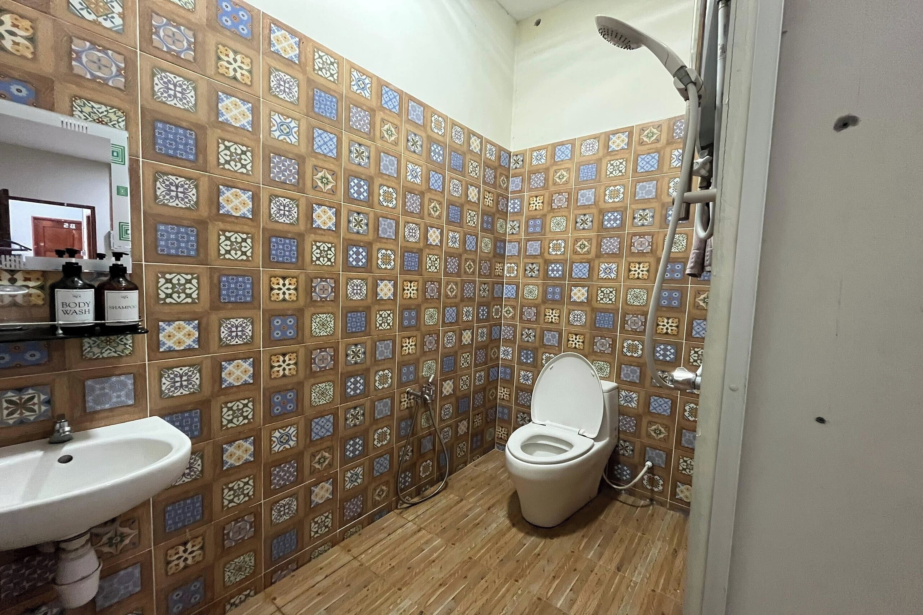 A bathroom with a tiled wall, a sink, a toilet, and a shower.