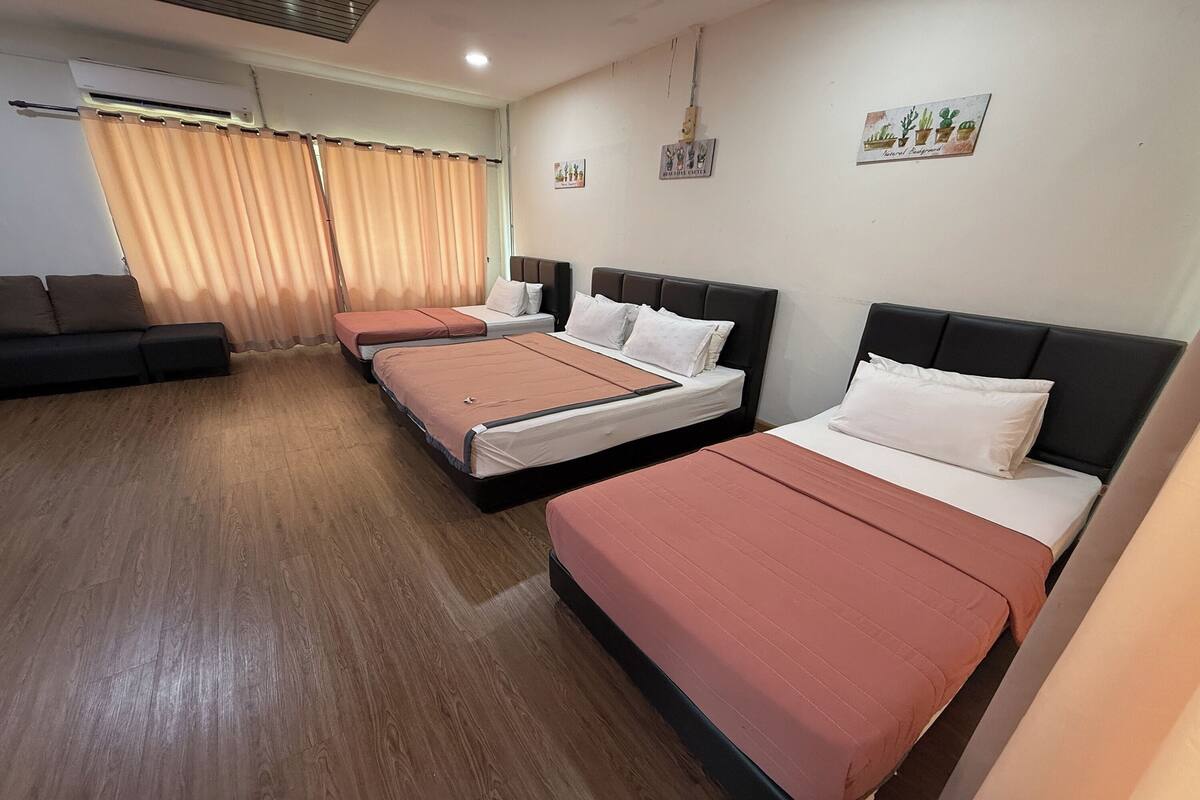 A hotel room with three single beds, a sofa, and a large window with curtains.