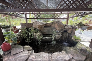 A rock garden with a water feature, surrounded by potted plants and a wooden pergola.