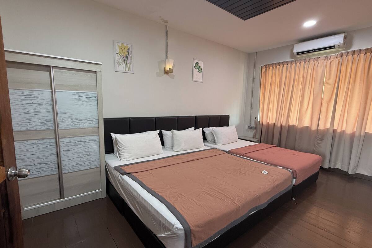 A hotel room with a large bed, a wardrobe with a glass door, an air conditioning unit, and a window with curtains.