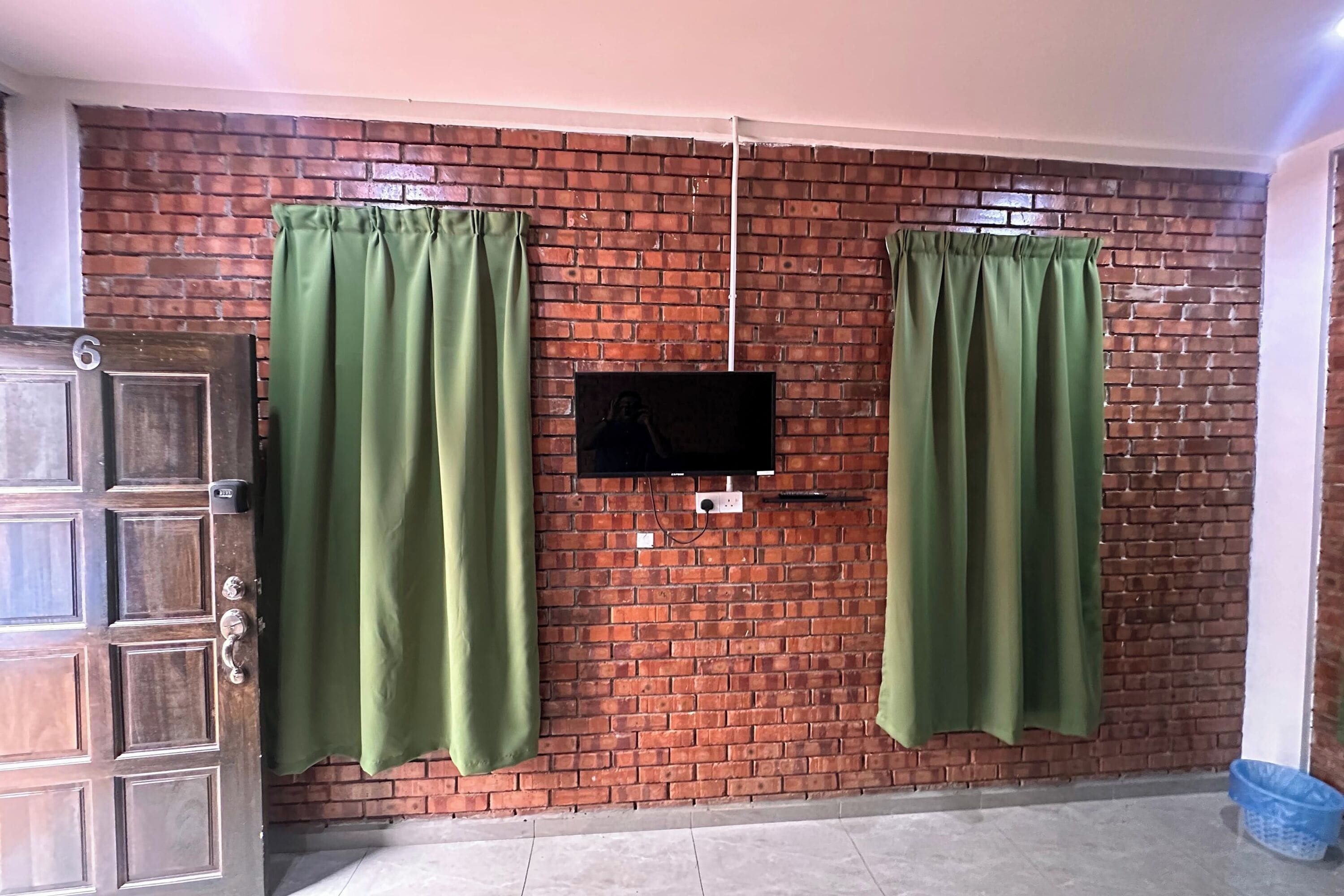 Una stanza con un muro in mattoni, una TV montata e due tende verdi.