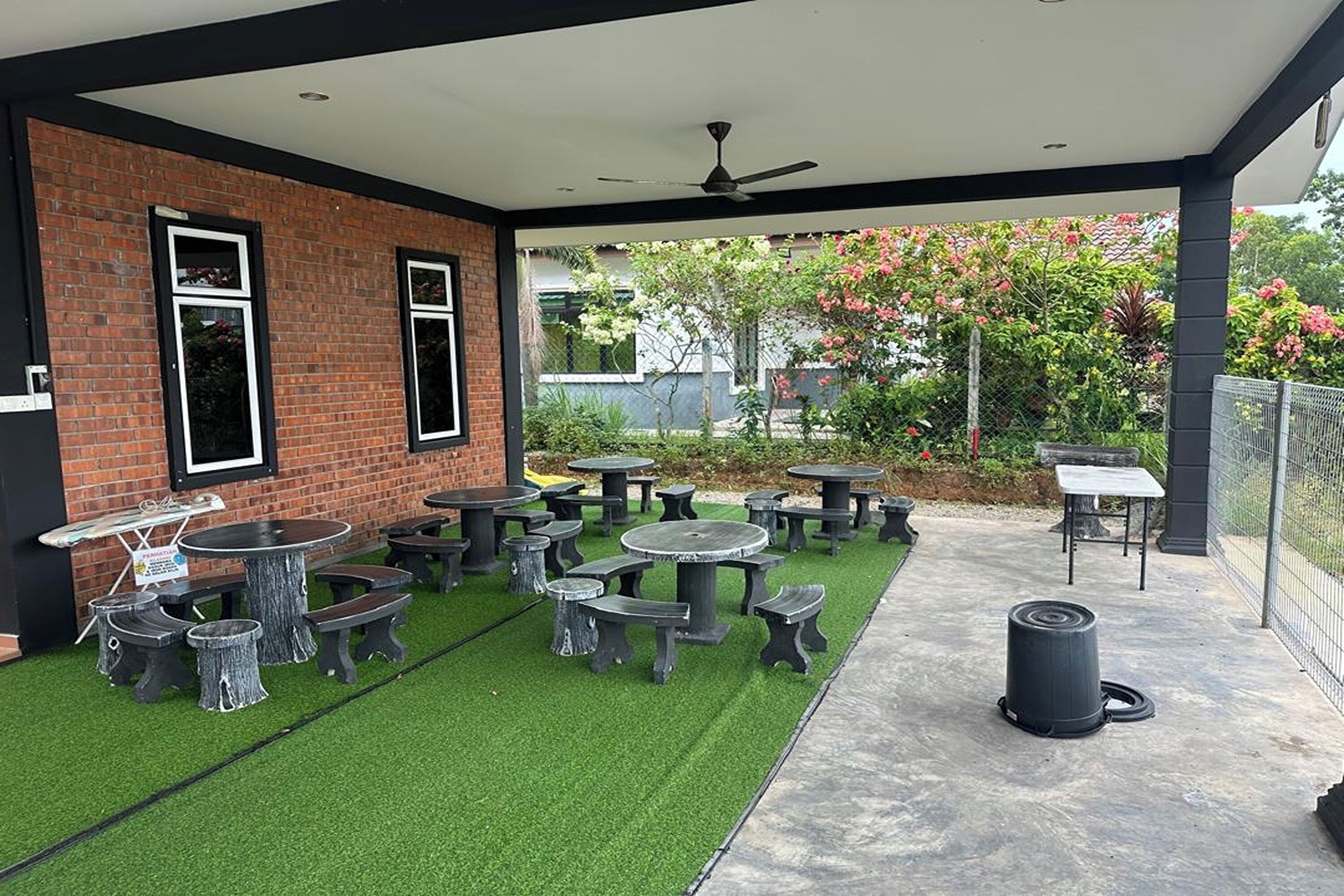An outdoor patio with multiple tables and benches, surrounded by a brick wall and a covered area with a ceiling fan.