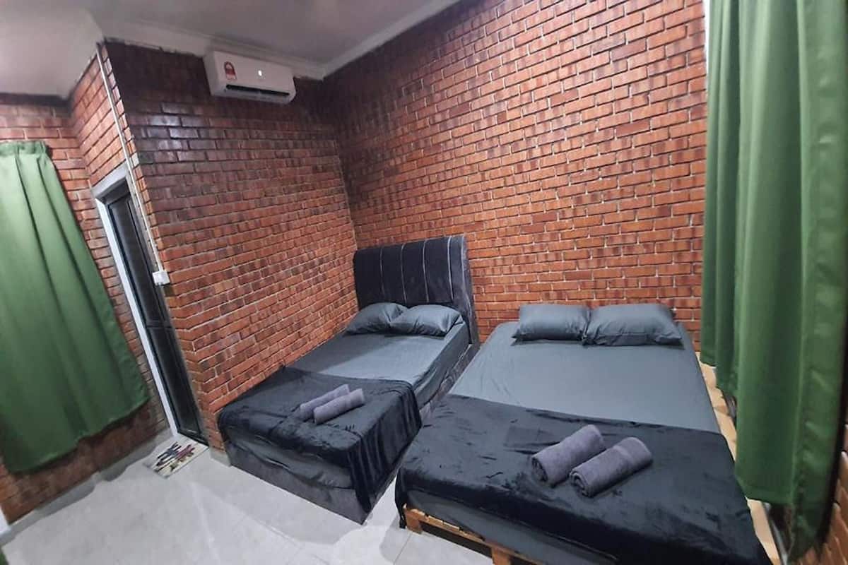 A small, enclosed room with brick walls, three single beds, and green curtains.