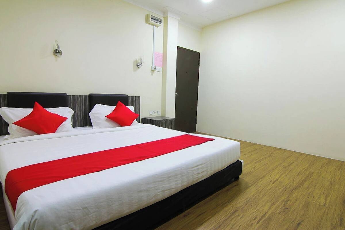 A hotel room with a large bed, two bedside tables, a wardrobe, and a wall-mounted thermostat.