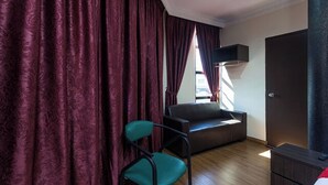 A room with a dark brown sofa, a teal chair, a wardrobe, and a window with curtains. - T P Hotel (Sitiawan)