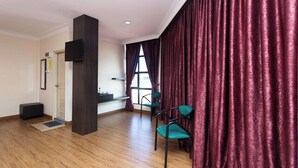 A hotel room with a wooden floor, a dark pillar, a flat-screen TV mounted on the wall, and a window with curtains. - T P Hotel (Sitiawan)