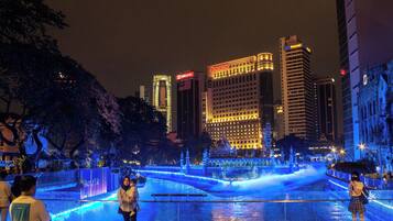 A nighttime cityscape with illuminated buildings and a water feature in the foreground.