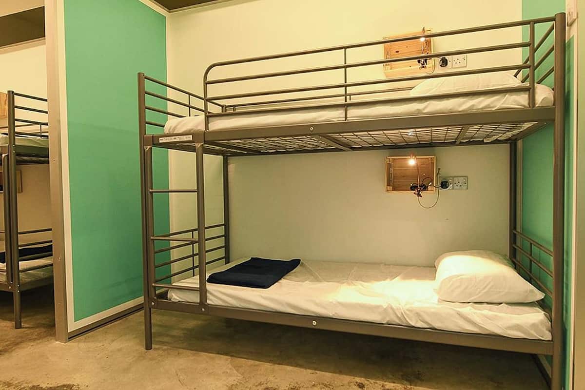 Une chambre avec un lit superposé, un mur vert, une prise de courant et une petite fenêtre.