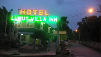 A hotel named "LUMUT VILLA INN" with a prominent neon sign, a staircase leading to the entrance, and a small outdoor seating area with tables and chairs.
