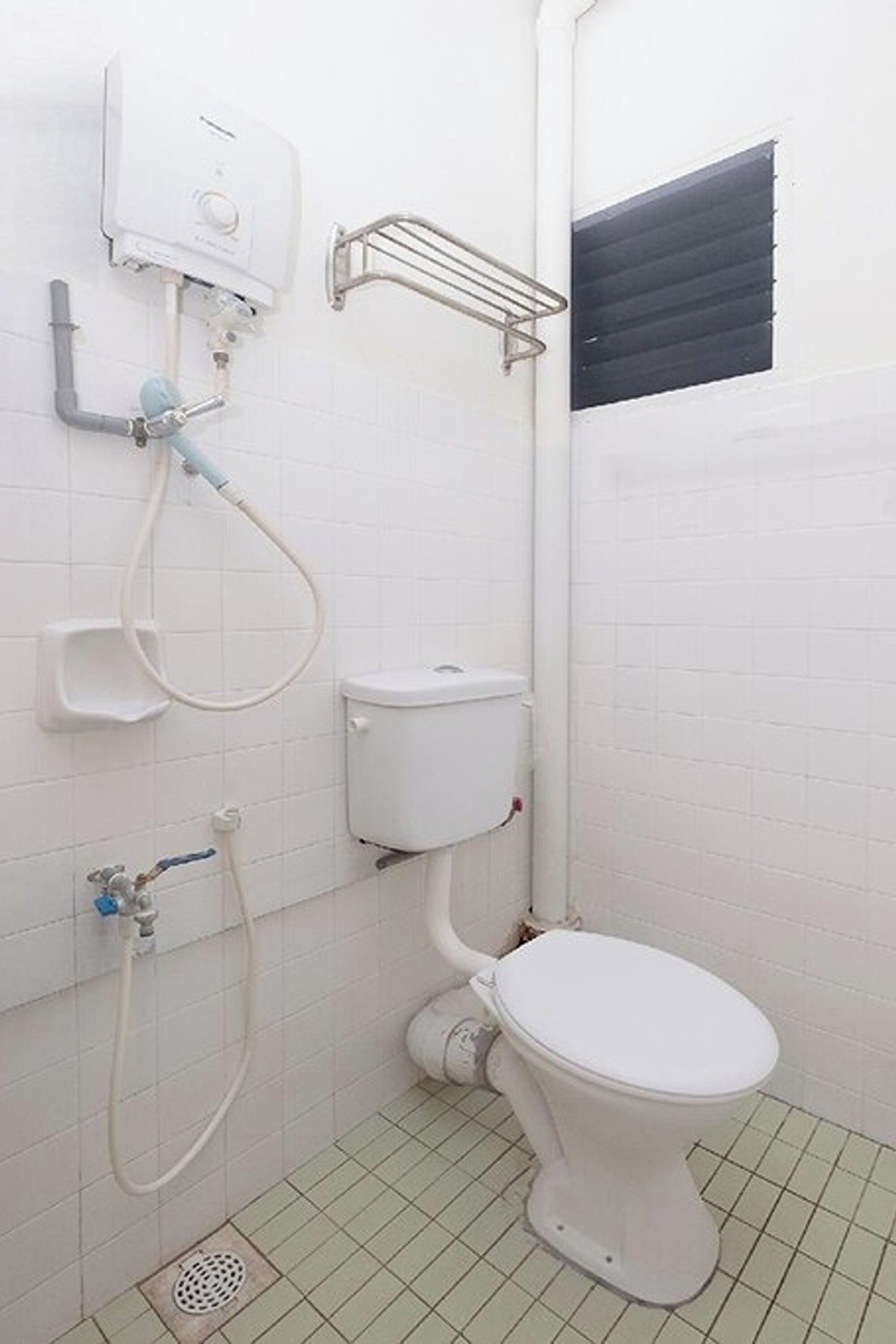 Een kleine, witte badkamer met toilet, douche en raam met zonwering.