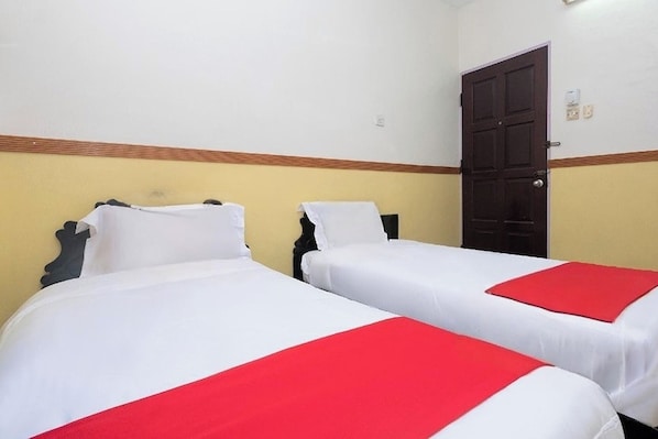 A room with two beds, each with white bedding and red accents, a wooden headboard, and a dark door. - Lumut Villa Inn (Lumut)