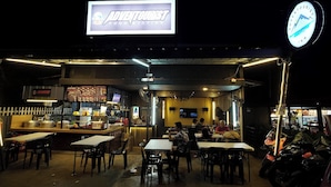 An outdoor seating area of a restaurant with tables and chairs, a counter with food items, and a sign that reads "ADVENTURIST HOOD STATION". - Adventourist Inn Coron (Coron)